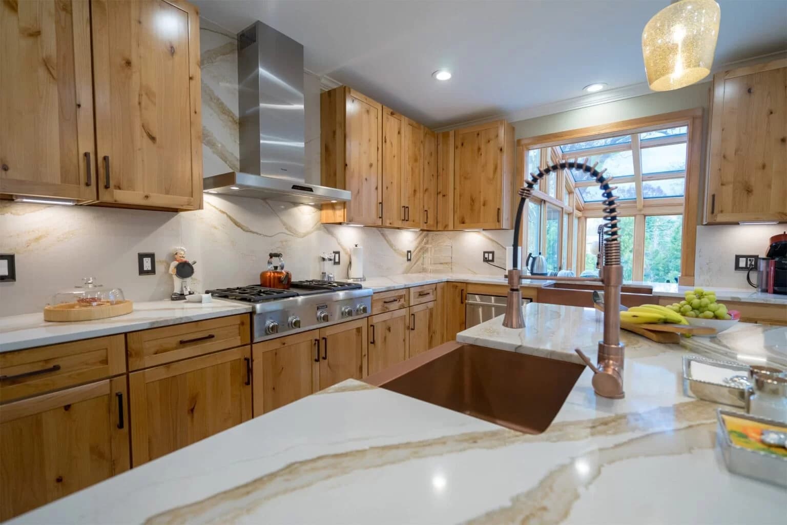 Finished kitchen with natural wood cabinetry, a quartz waterfall island and a copper sink